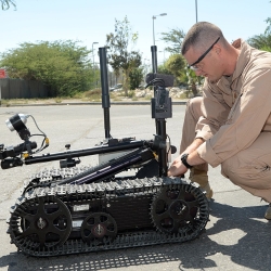 A photo of a service member preparing a small autonomous robot.